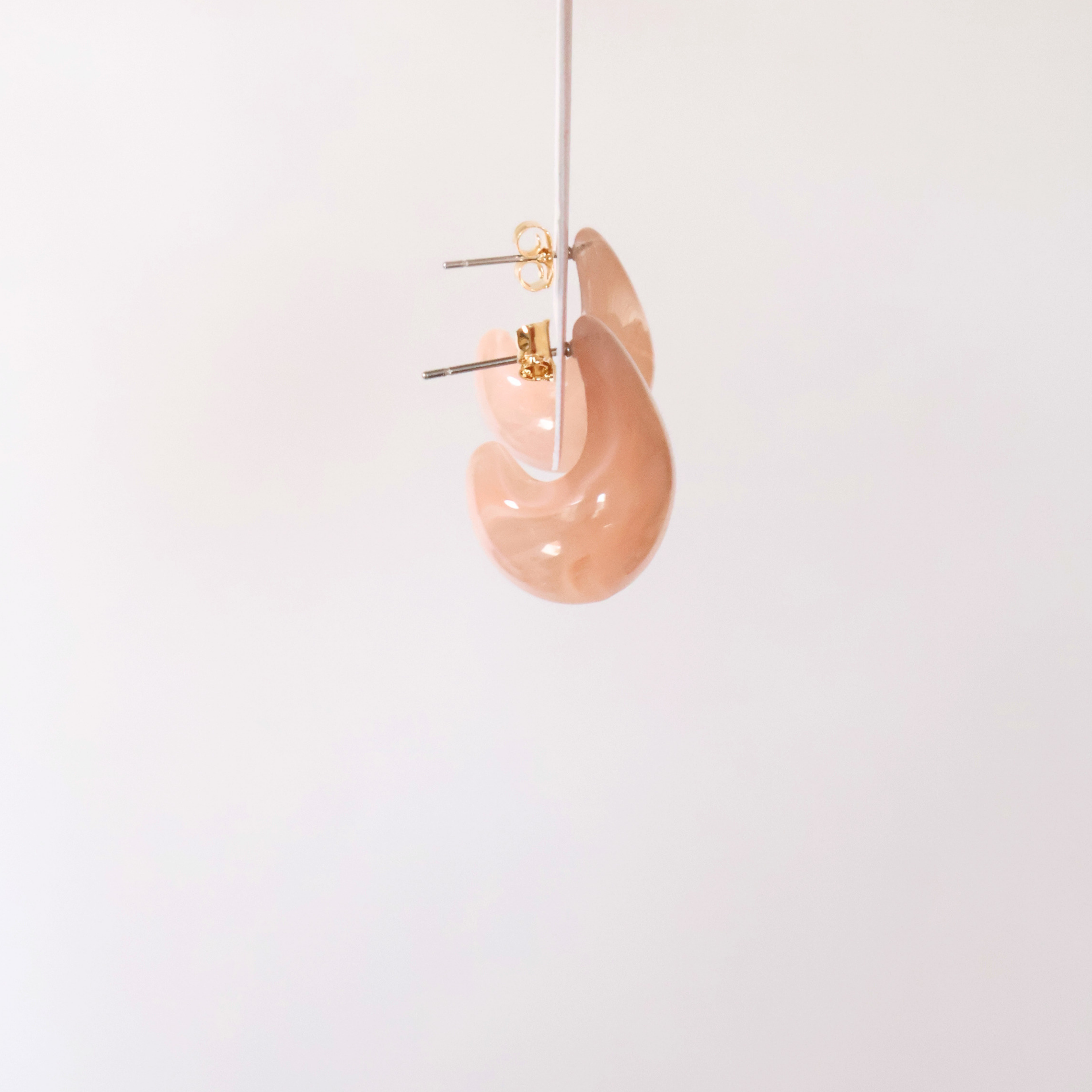 Side view of peachy pink teardrop shaped earrings to show shape on a white backdrop