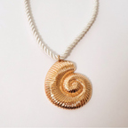 close up view of cream rope and brassy metal necklace with metal shell pendant displayed on a white background