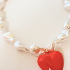 Close up of faux baroque pearl necklace with a red heart pendant on a white background