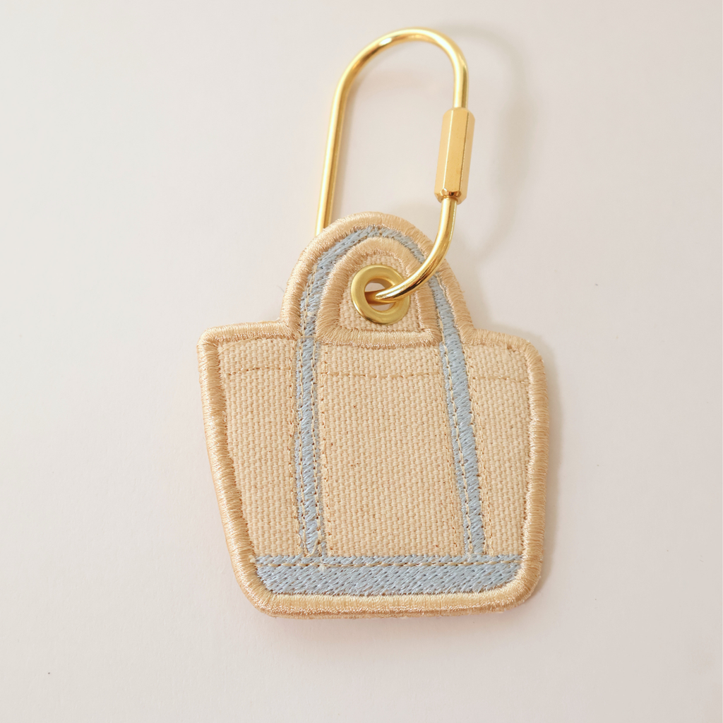 Light blue bag shaped bag charm on a white background