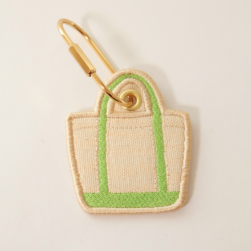 Green bag shaped bag charm on a white background