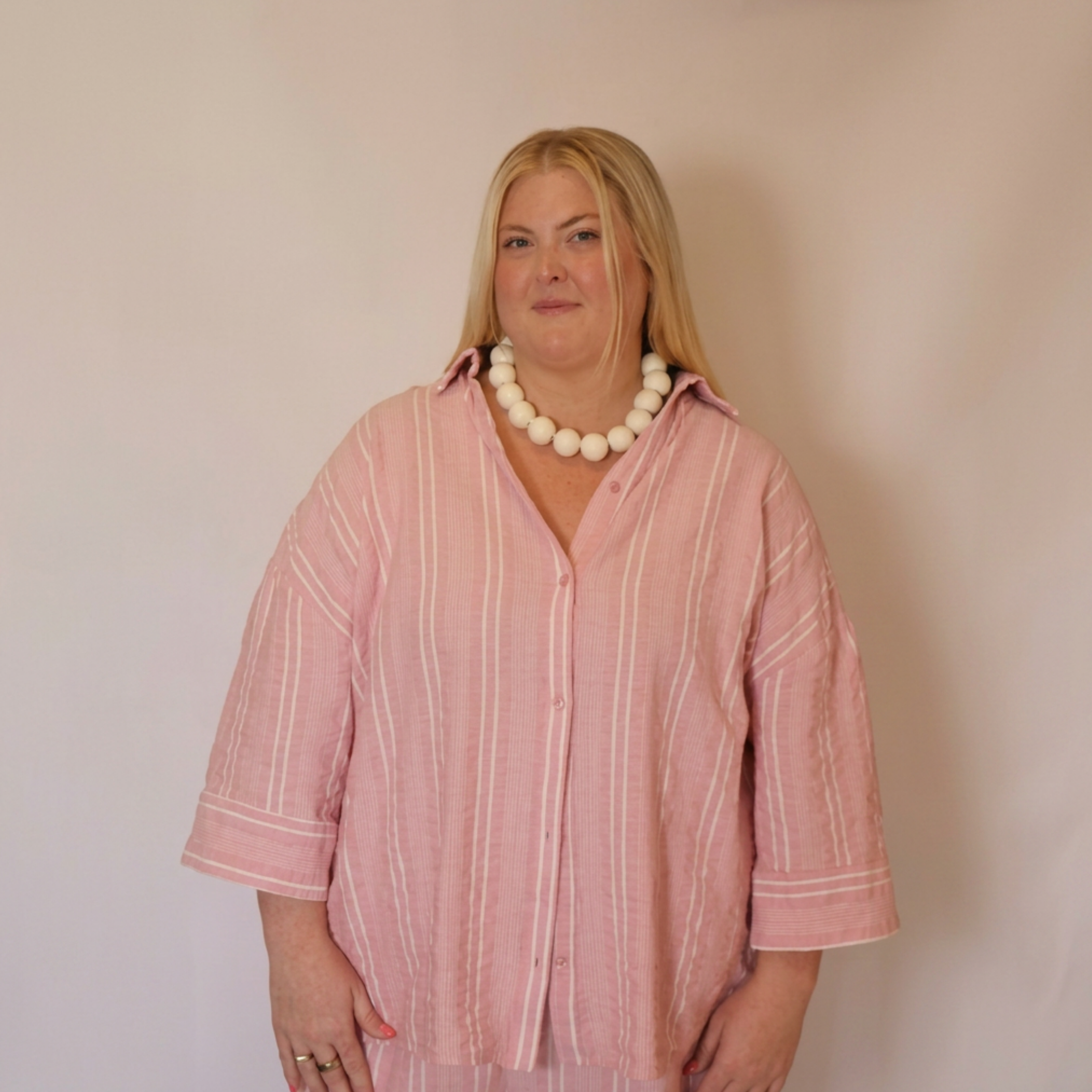 Woman facing forward wearing the Azalea button down shirt and a large beaded necklace. The photo shows from the waist up.
