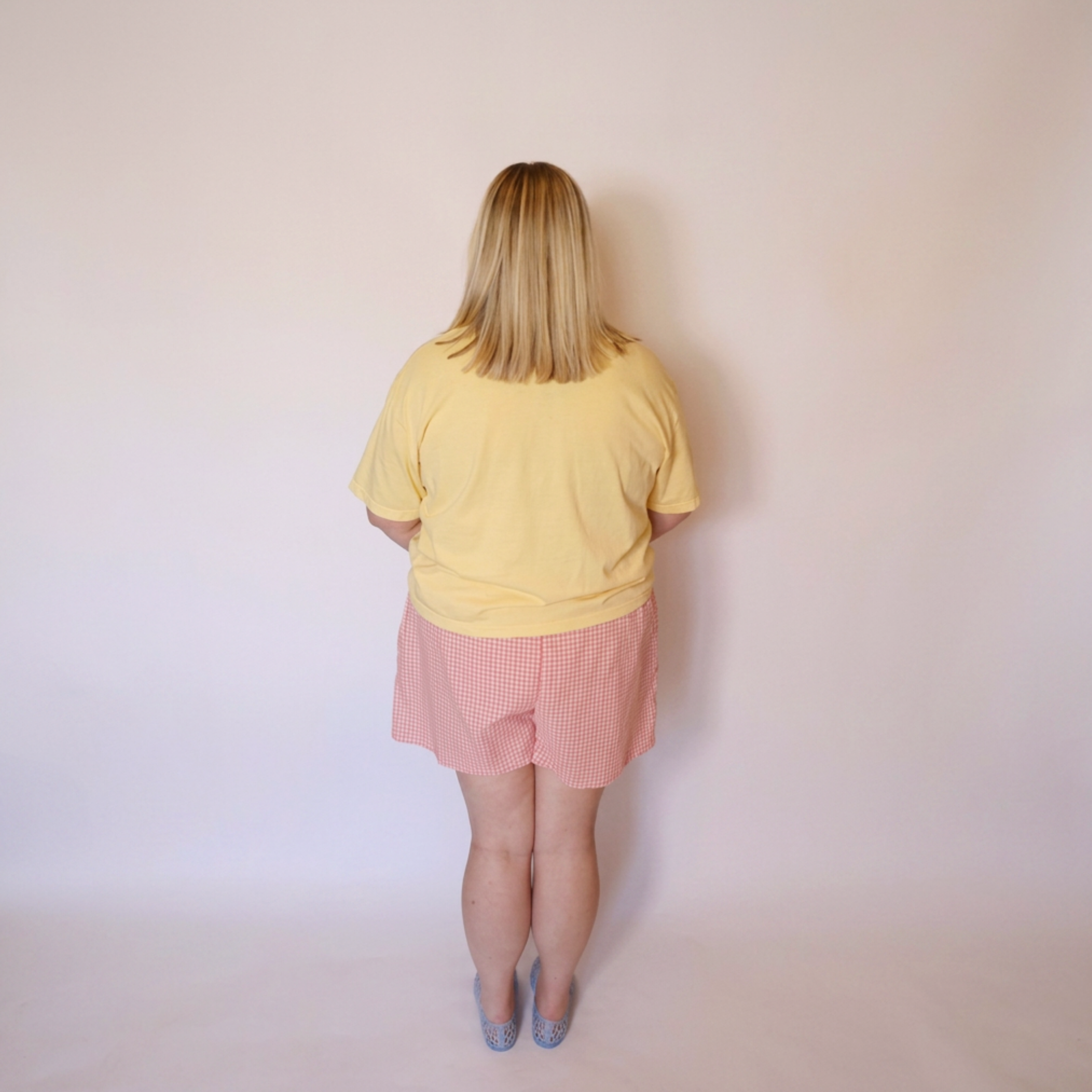 Woman wearing a yellow T-shirt and the Tansy pink gingham cotton shorts facing backwards for the back view