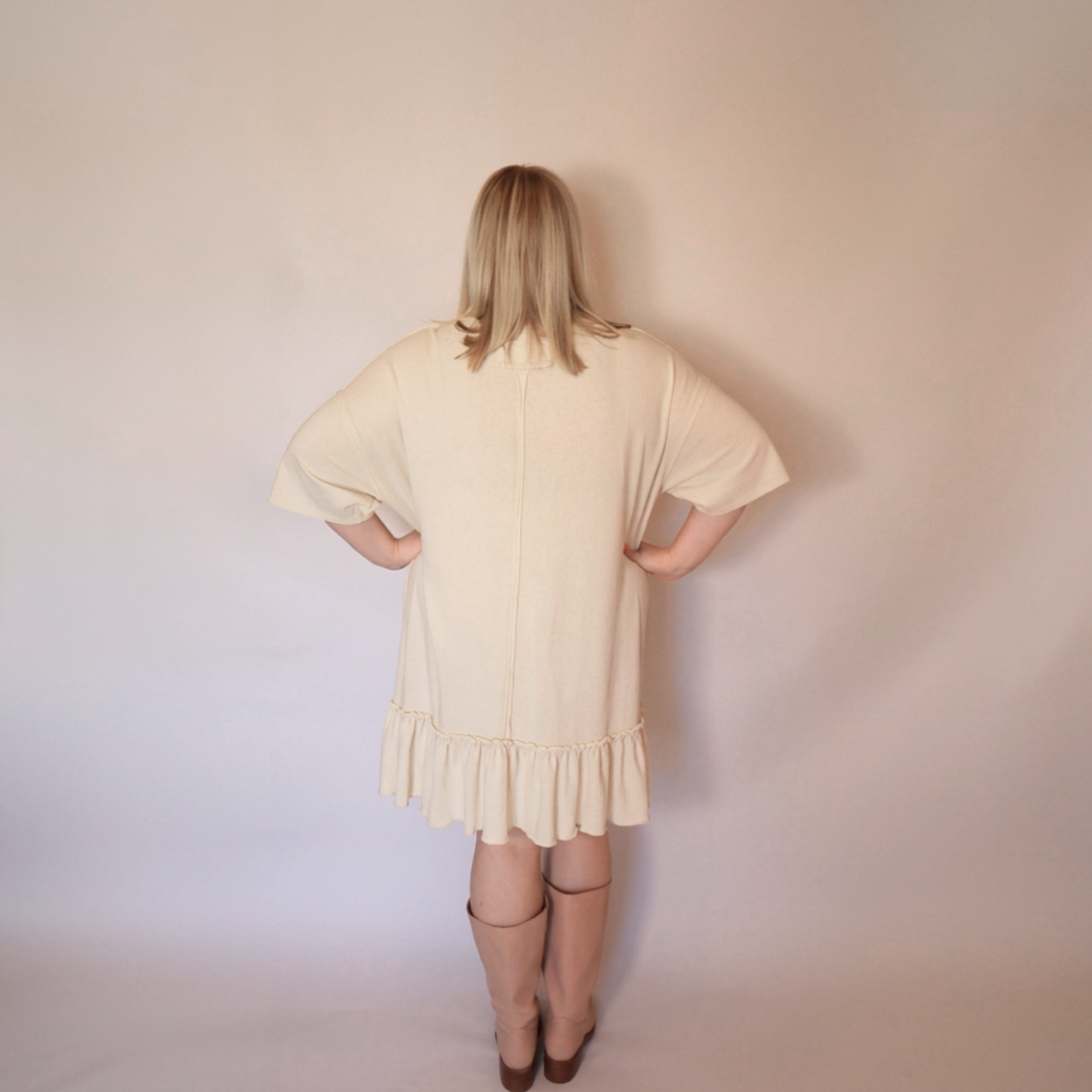 Woman facing backwards wearing the cream laurel dress and tall pink boots.