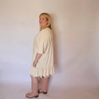Woman facing left wearing the cream laurel dress and tall pink boots.