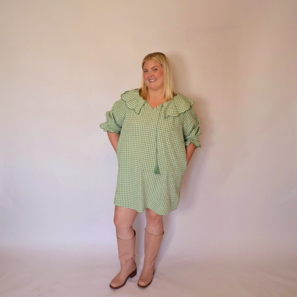 Woman facing forward wearing the Green Gingham Louisa Dress and pink boots and her hands in the pockets